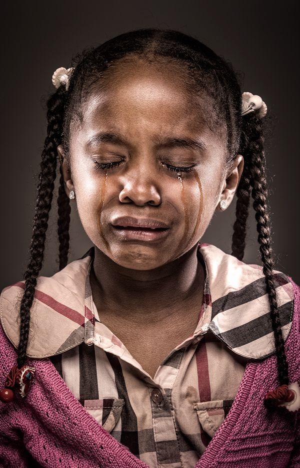 A young Ghanaian girl with braided hair weeping with her eyes closed