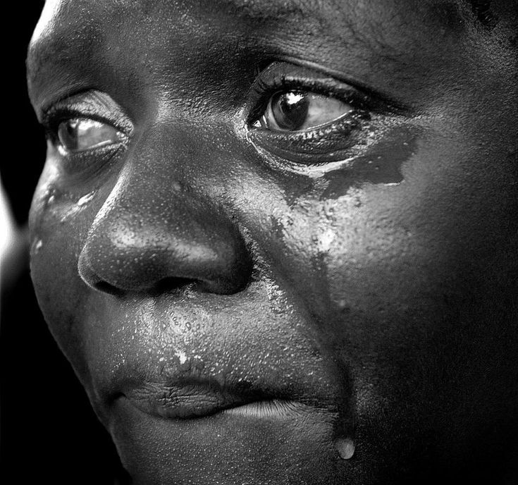 A monochrome close-up of a Ghanaian woman with tears on her cheek, gaze held to the side